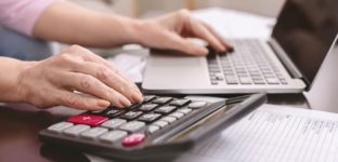 Mulher fazendo conta com calculadora e notebook, simulando a criação do IR