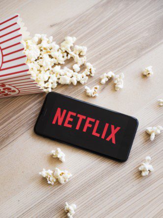 Pipoca derrubada ao lado de um celular com a logo da Netflix na tela, ilustrando o tema: história da netflix