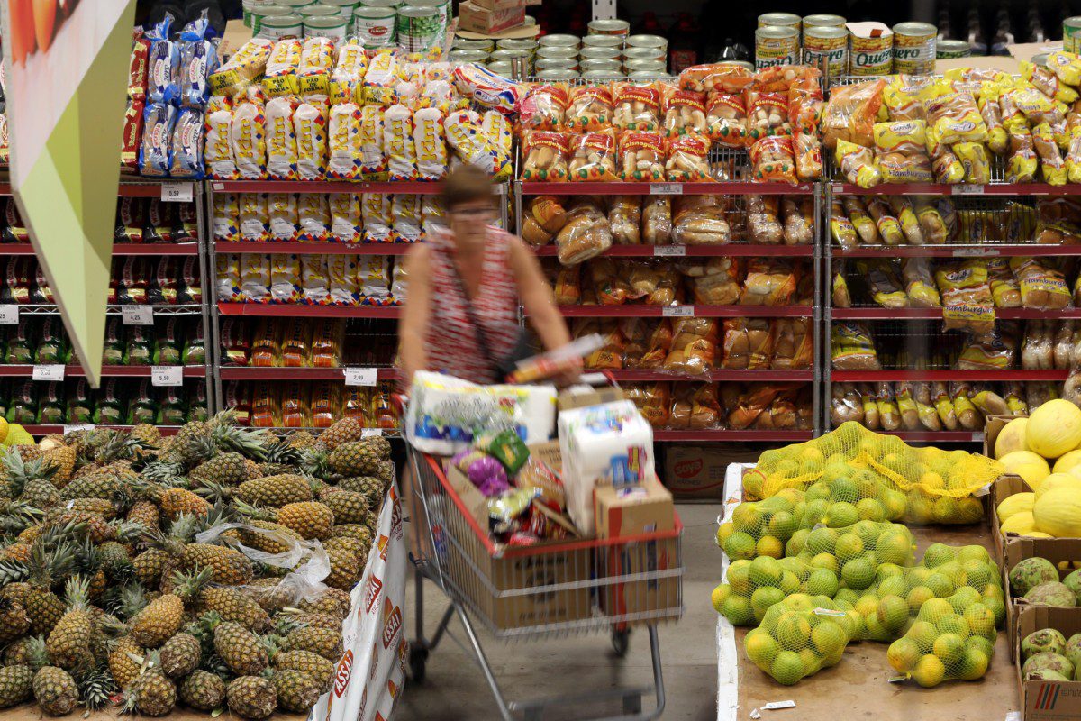 Mulher empurra um carrinho de compras em um supermercado, onde o preço dos produtos é impactado pelo IPCA.