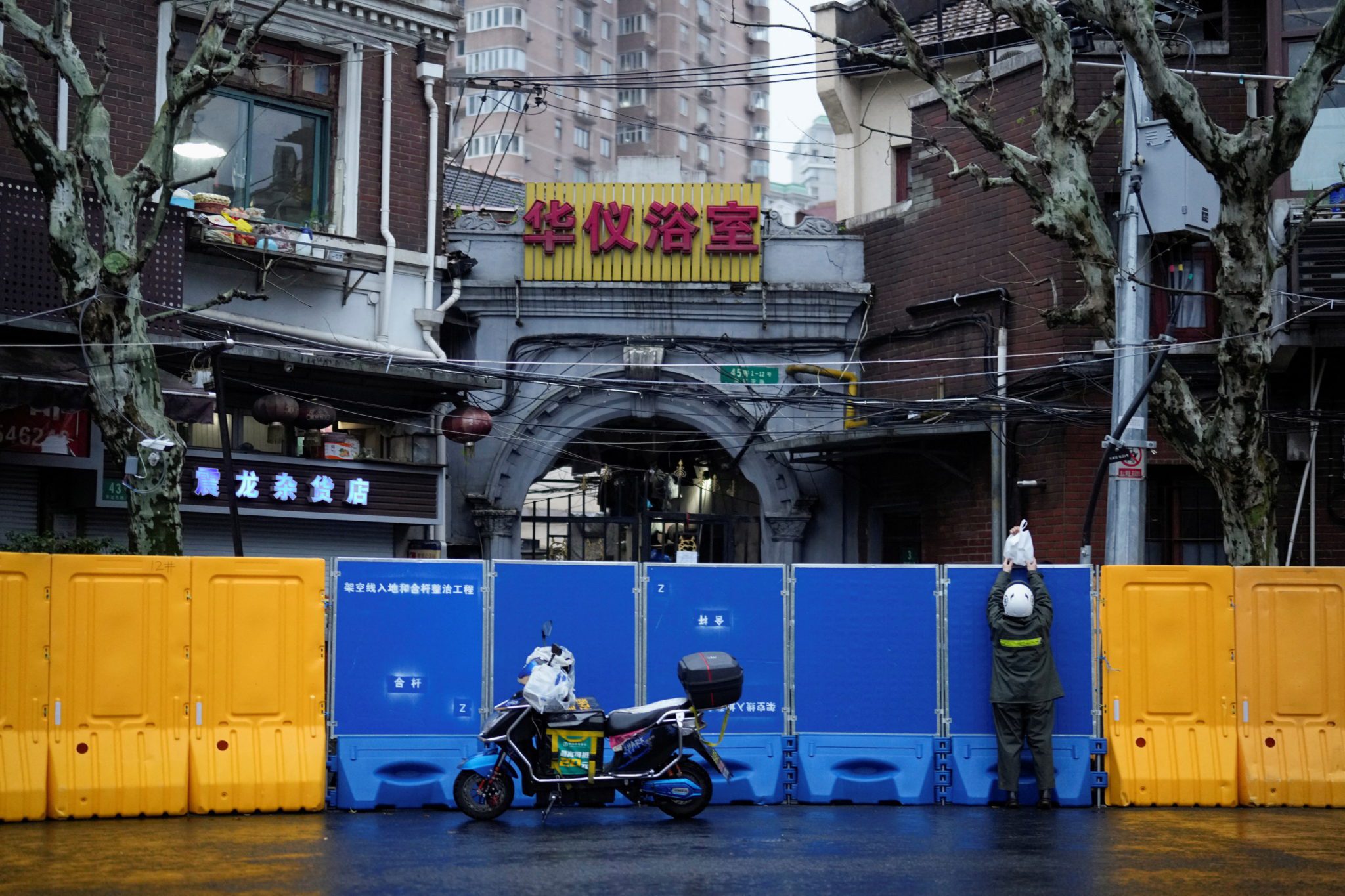 Entregador passa mercadorias para uma pessoa sobre as barreiras de uma área em lockdown em meio à pandemia de Covid-19 em Xangai
