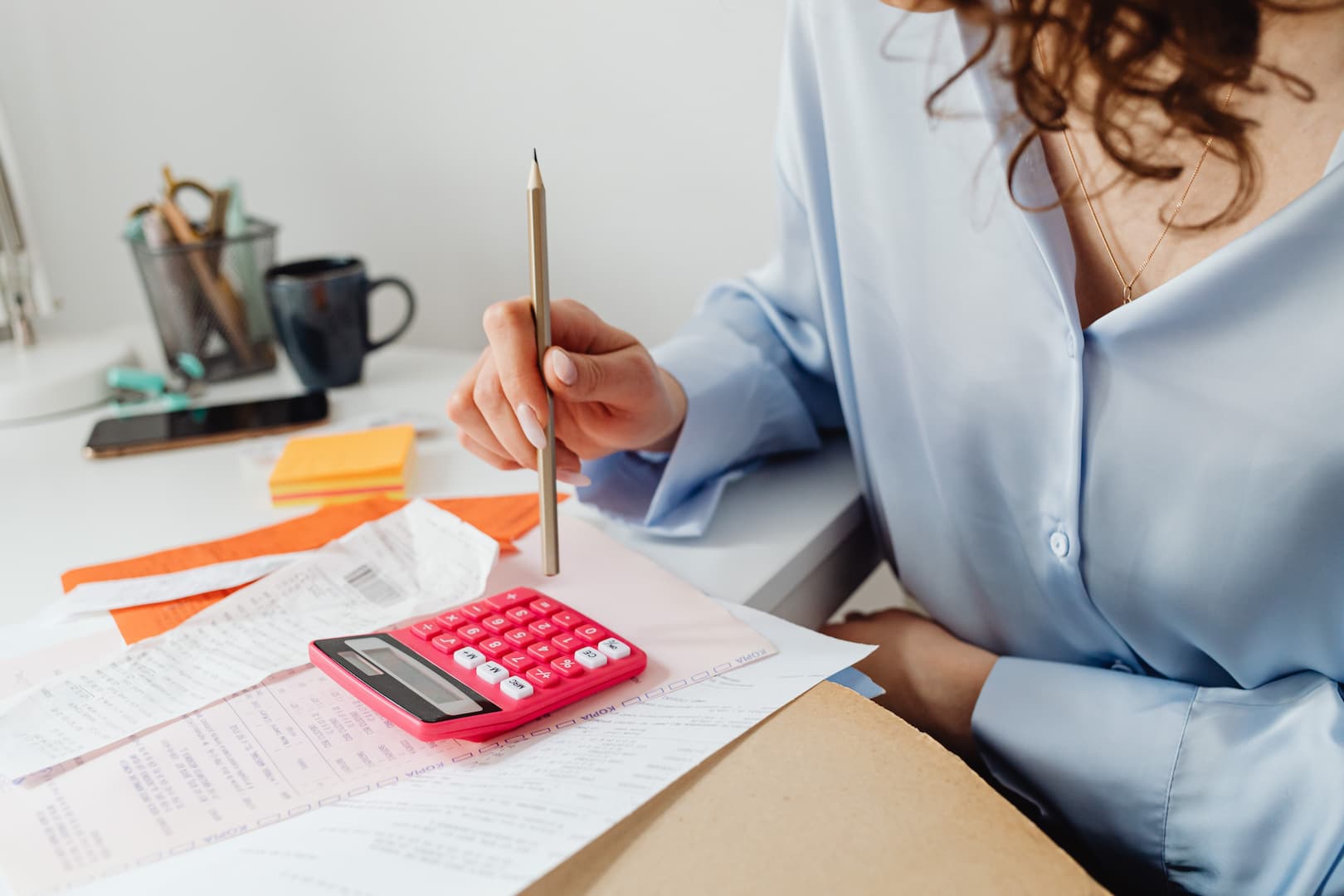 Mulher com lápis na mão e calculadora na mesa, fazendo contas