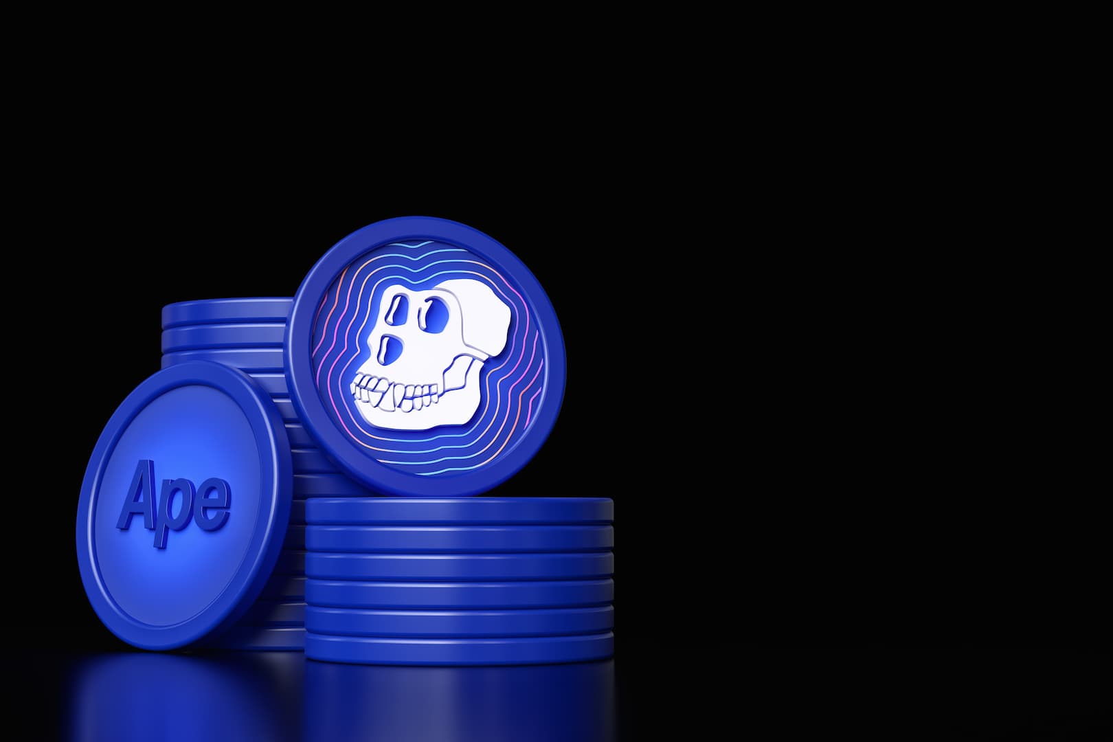 A imagem mostra duas pilhas de moedas azuis, representando a ApeCoin, em frente a um fundo preto. Há uma moeda estampada com o desenho de um crânio de macaco posta de pé em cima de uma das pilhas. Encostada na outra pilha, há uma moeda com o dizer “Ape”.