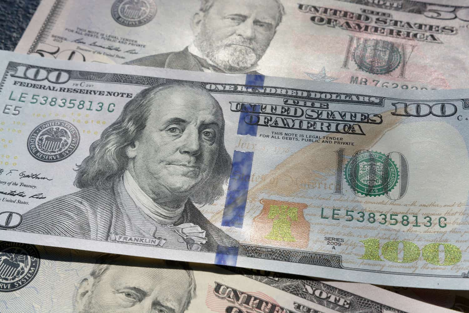 A imagem mostra uma nota de 100 dólares, posicionada acima de duas notas de 50 dólares. (Foto: Unsplash / Colin Watts)