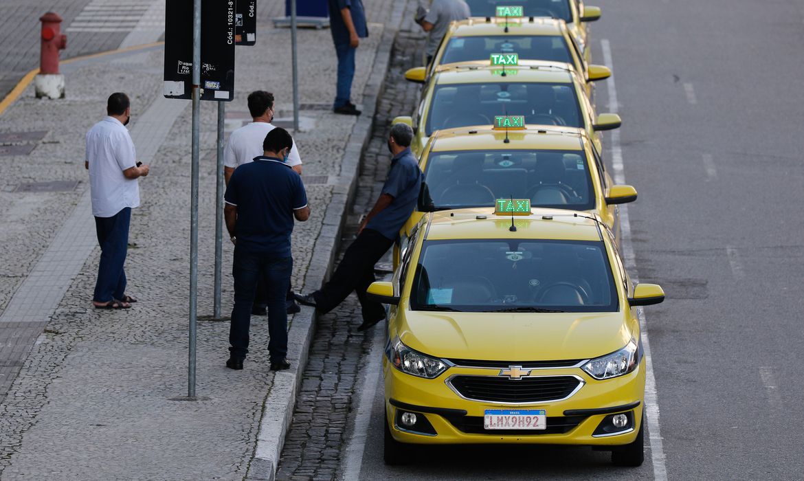 taxistas encostados nos carros em ponto de taxi