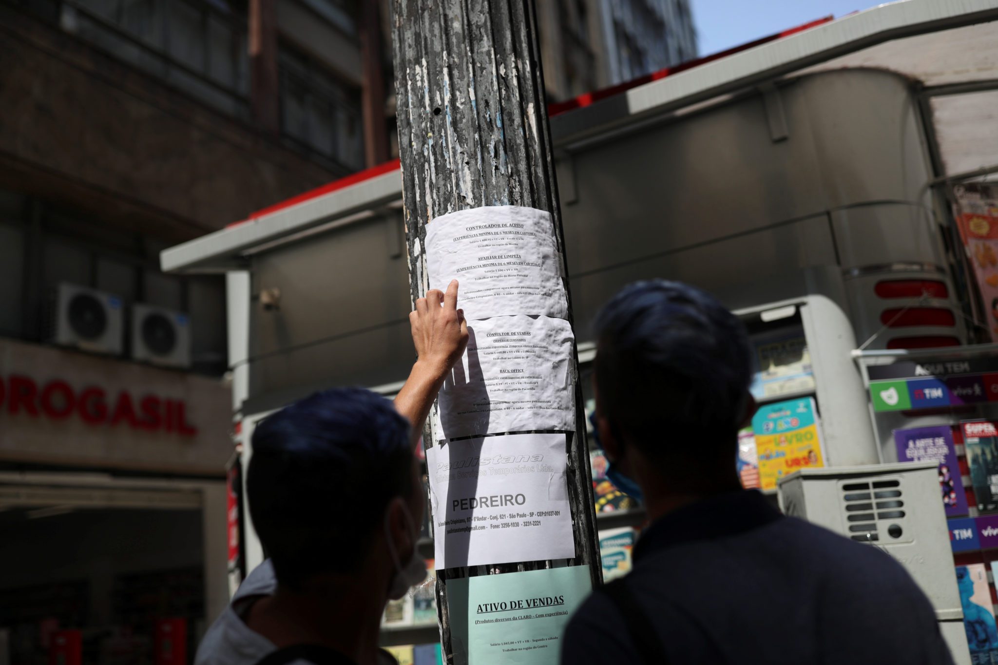 pessoas vendo cartaz com anuncios de emprego pregado em um poste na rua