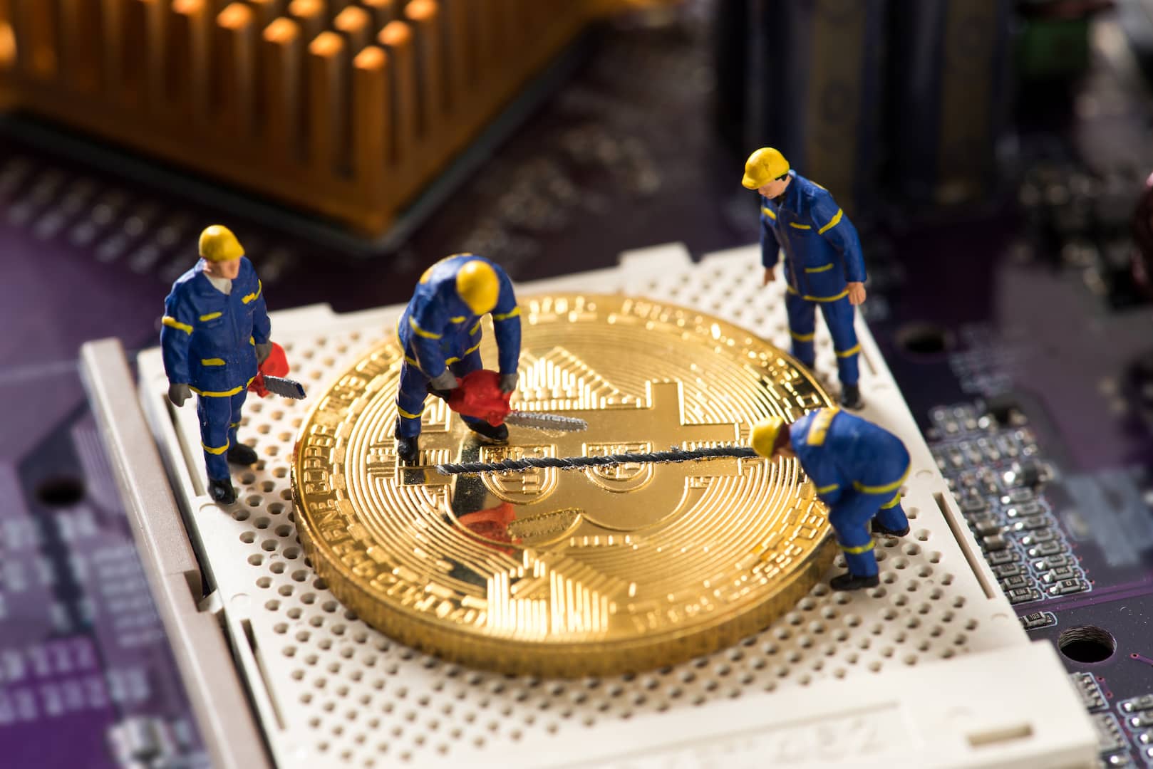 A imagem mostra uma moeda que simboliza o bitcoin em cima do que parece ser uma placa de computador. Há quatro bonecos, vestidos com macacões azuis e chapéus amarelos, serrando a moeda ao meio, ilustrando o processo de halving. (Imagem: Shutterstock / PowerUp)