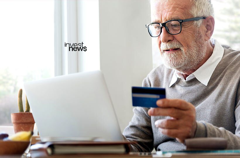 idoso segurando um cartão de crédito em frente a um notebook para fazer compras online