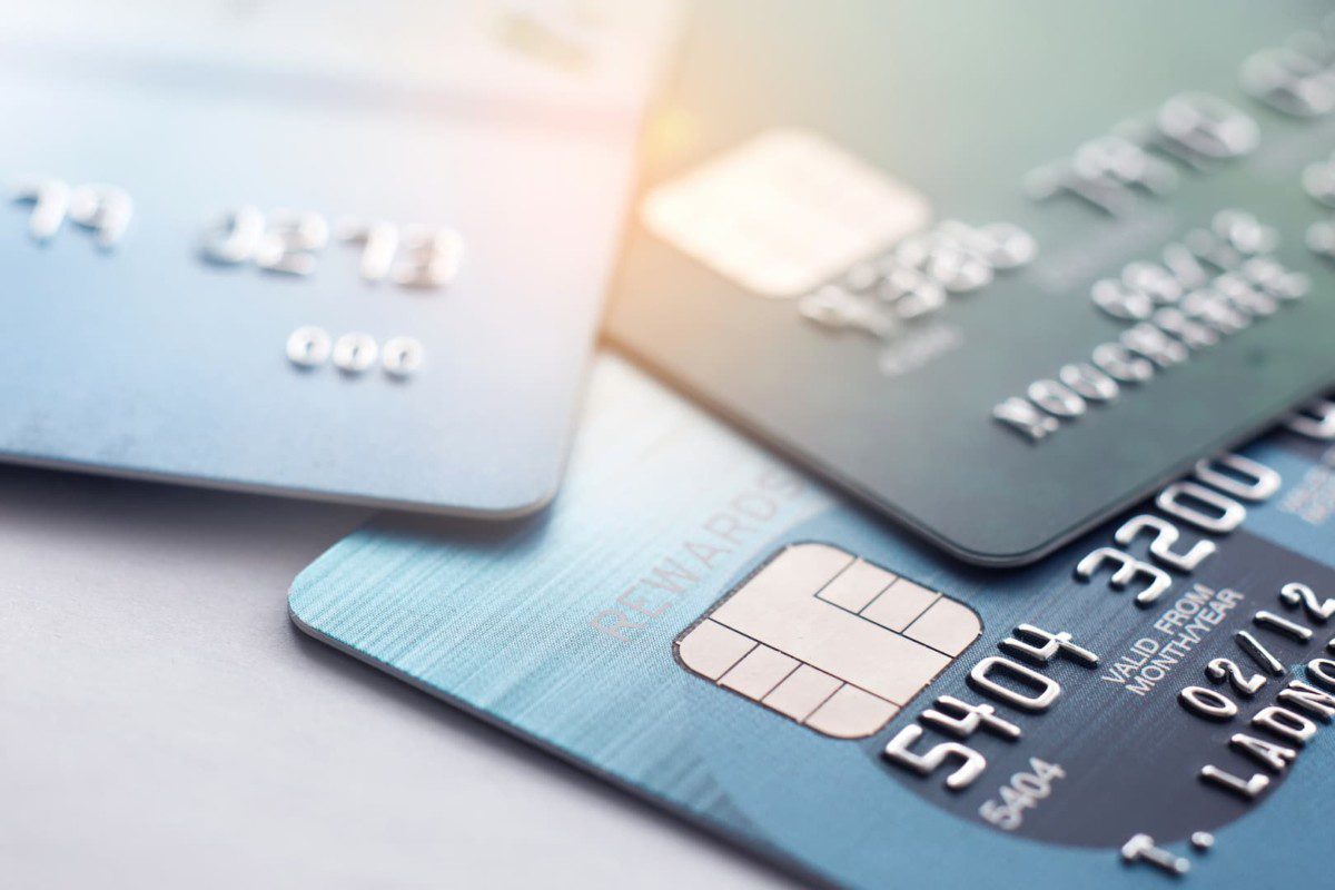 A imagem mostra um close up de três cartões de crédito em cima de uma superfície cinza. (Foto: Shutterstock / Teerasak Ladnongkhun)