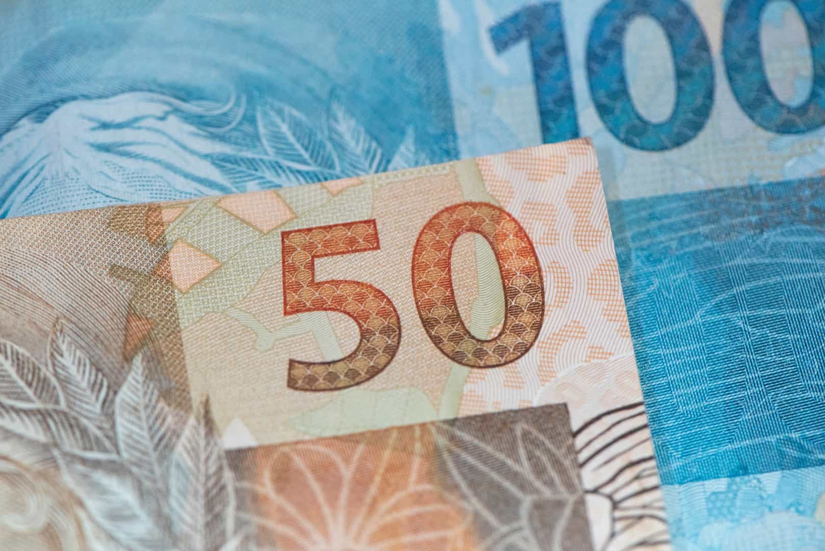 A imagem mostra uma nota de R$ 50,00 em cima de uma nota de R$ 100,00. (Foto: Shutterstock / Paulo R Korb)