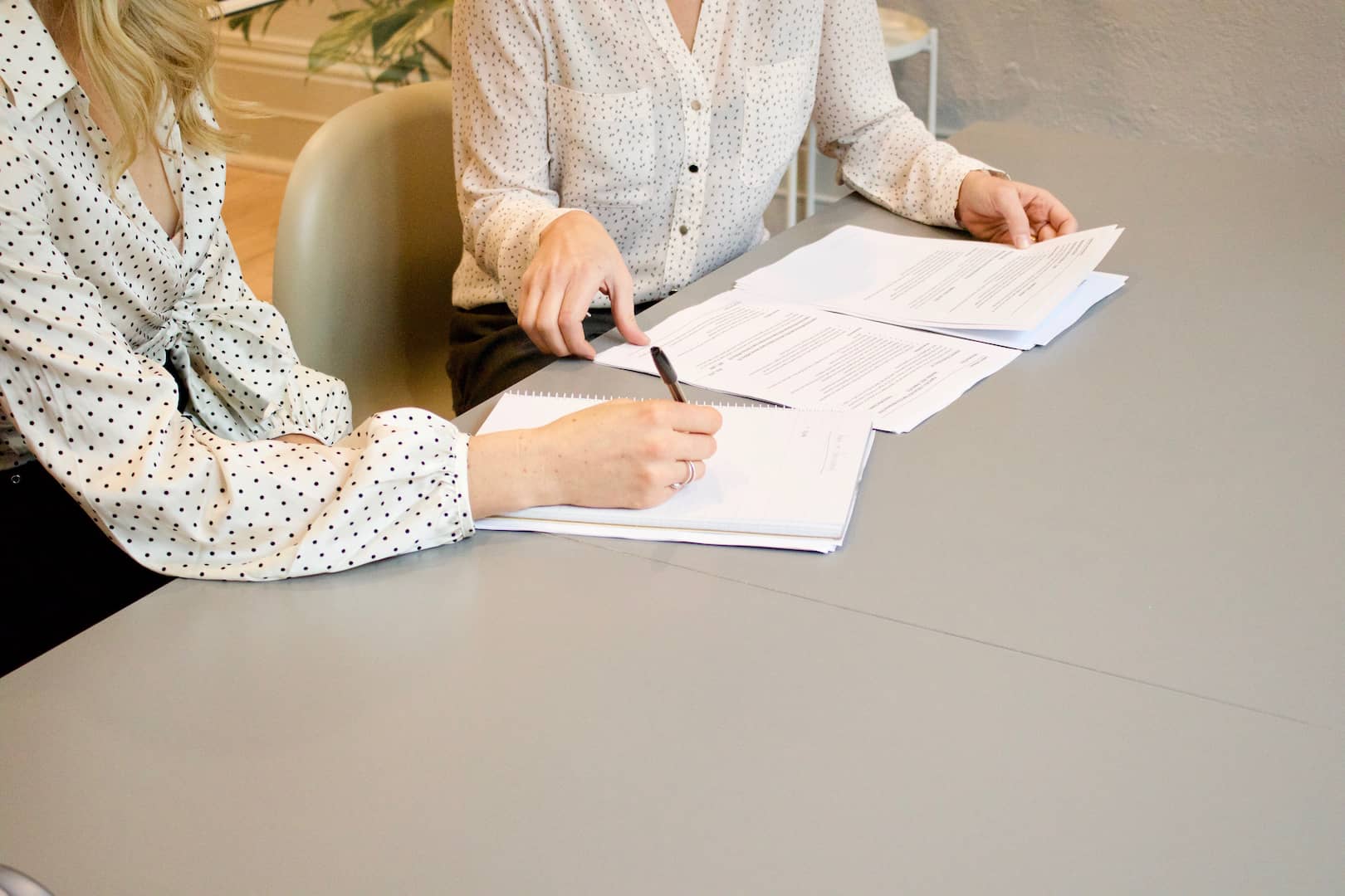 A imagem mostra duas mulheres sentadas em uma mesa. Uma delas assina um contrato como exemplo do funcionamento do mercado a termo.