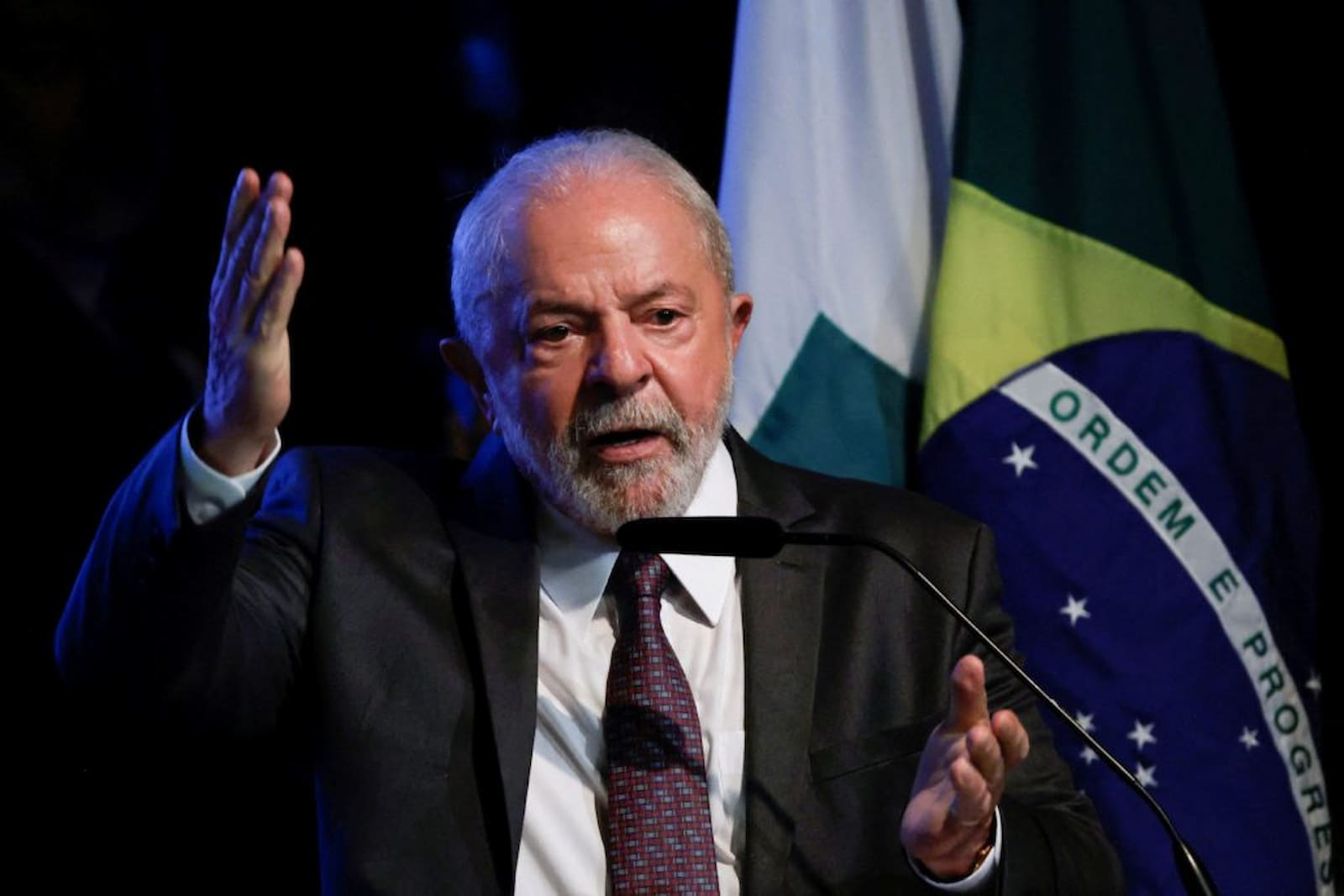 Presidente Lula falando ao microfone com a mão direita levantada