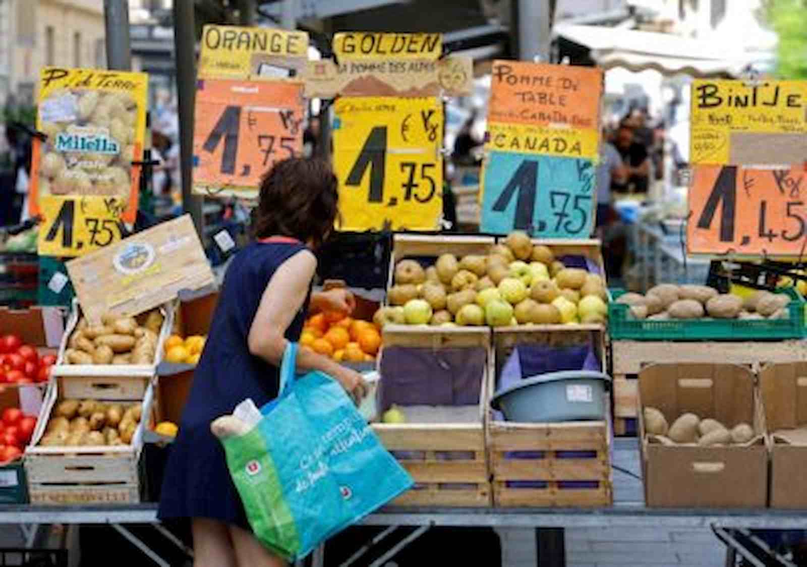 mulher em um mercado de ruas comprando frutas com seus respectivos preços acima