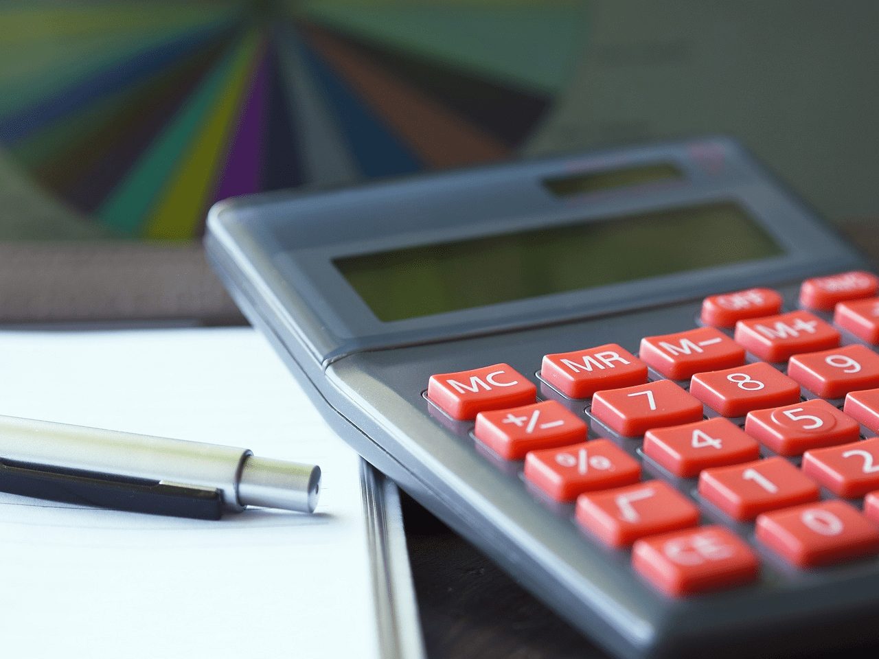 Uma calculadora ao lado de um lápis e um caderno, calculando gastos pessoais mensais