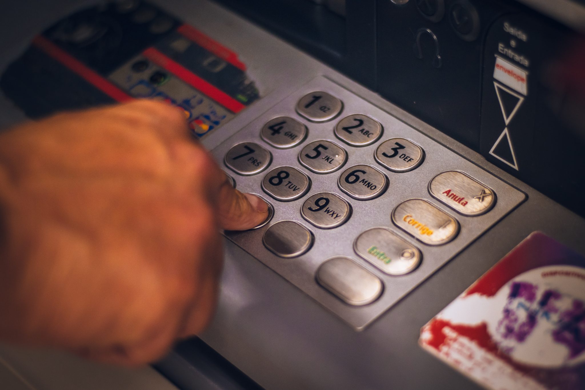 Foto focada nos números de um caixa eletrônico, com um dedo pressionando uma das teclas