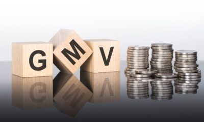 cubos de madeira formando a sigla "GMV" ao lado de 3 pilhas de moeda