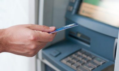 Mão segurando cartão em frente a uma máquina bancária