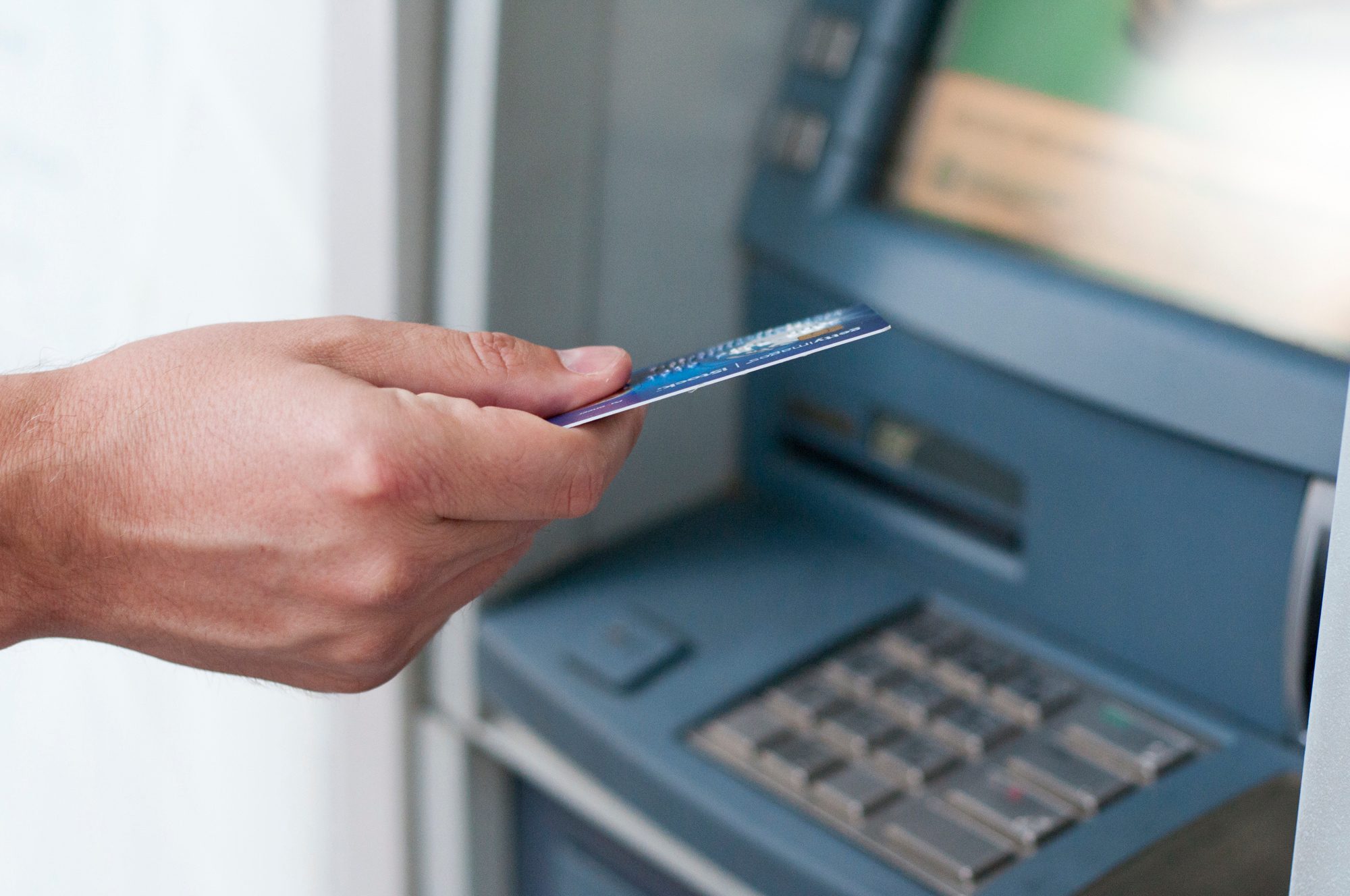 Mão segurando cartão em frente a uma máquina bancária