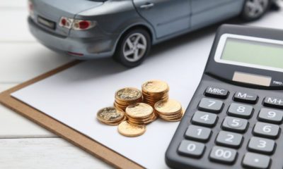 miniatura de um carro ao lado de uma pilha de moedas e uma calculadora, com uma prancheta embaixo. A imagem ilustra o ITCMD