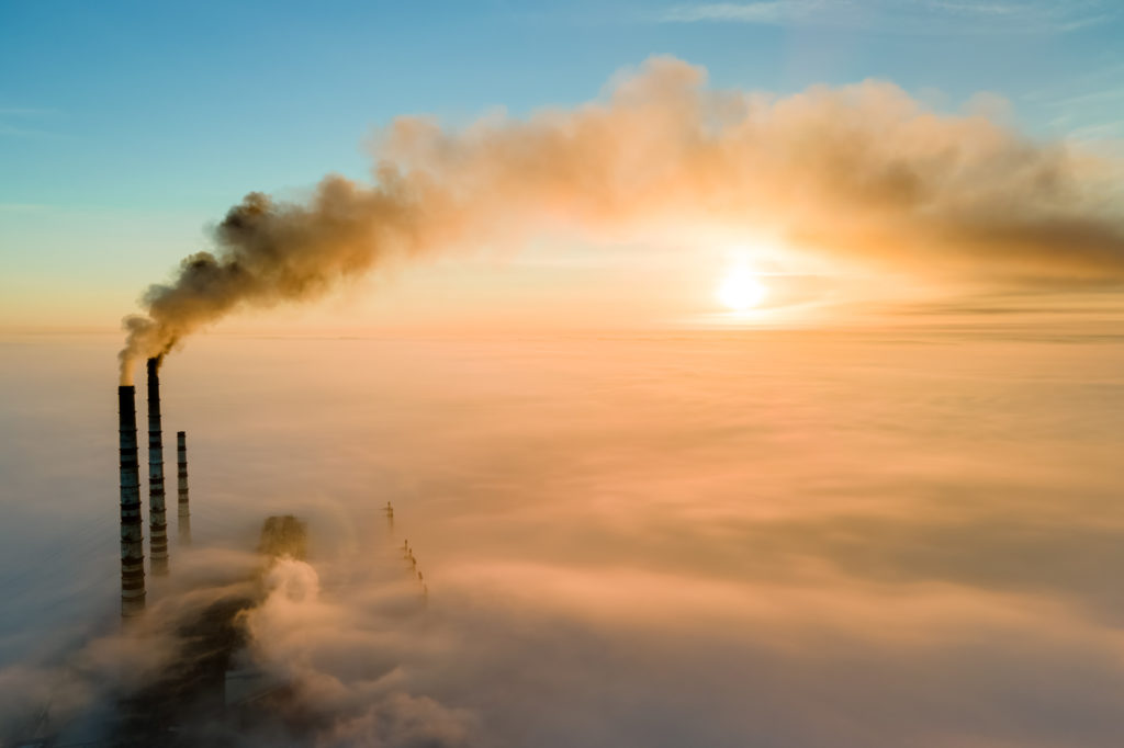 Aerial view of coal power plant high pipes with black smoke moving up polluting atmosphere at sunset.