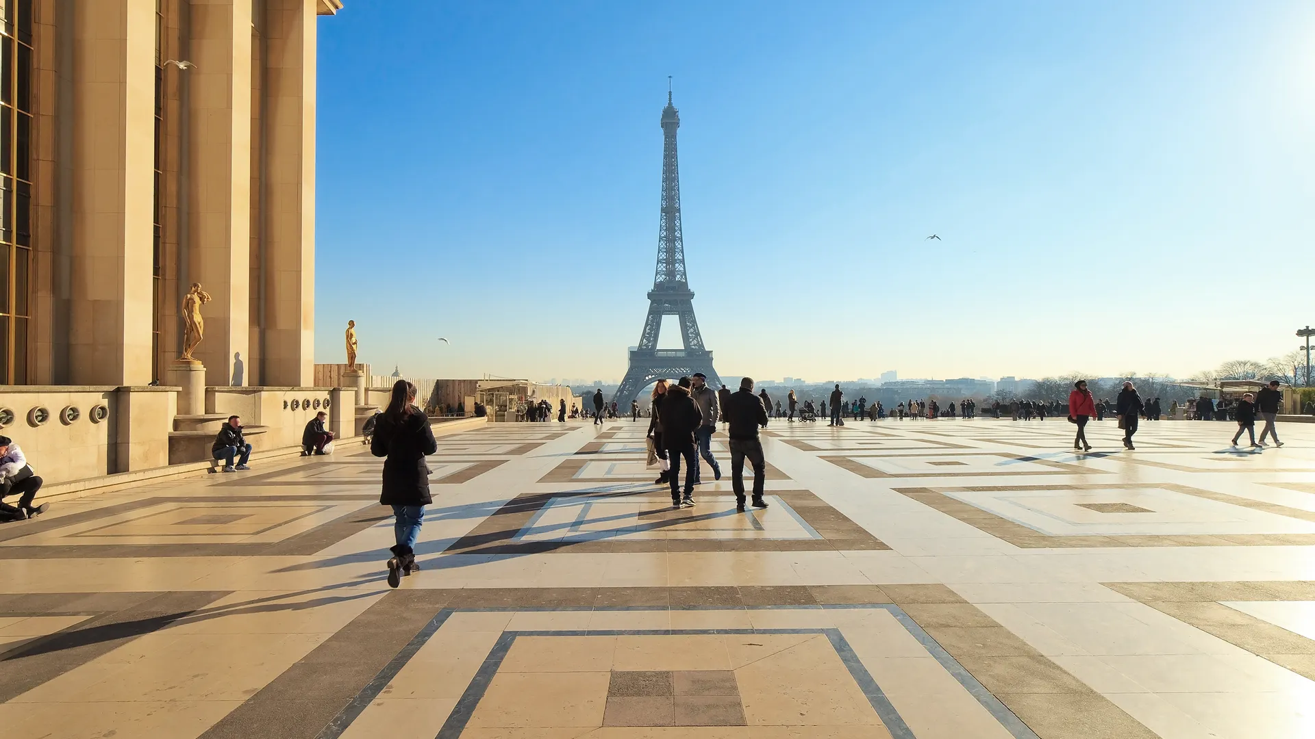 Turistas caminham pela Esplanada no Trocadéro, com vista para a Torre Eiffel em Paris, França