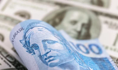 detalhe de uma nota de cem reais do Brasil, presa entre notas de 100 dólares americanos