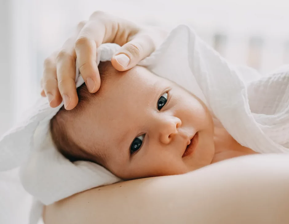 Bebê branco de olho azul no colo da mãe envolto em um cobertor; natalidade; nascimento