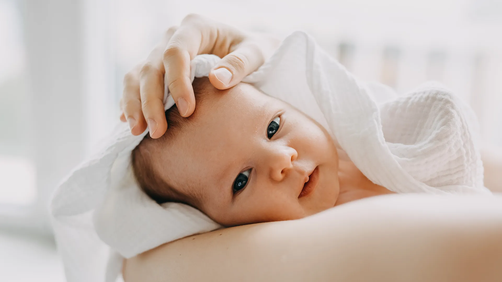 Bebê branco de olho azul no colo da mãe envolto em um cobertor; natalidade; nascimento