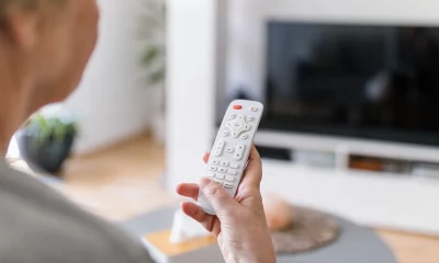 Mulher idosa segurando um controle remoto em frente à TV