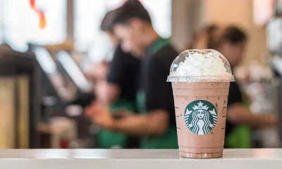 Balcão de loja da Starbucks com café em primeiro plano e funcionários em segundo