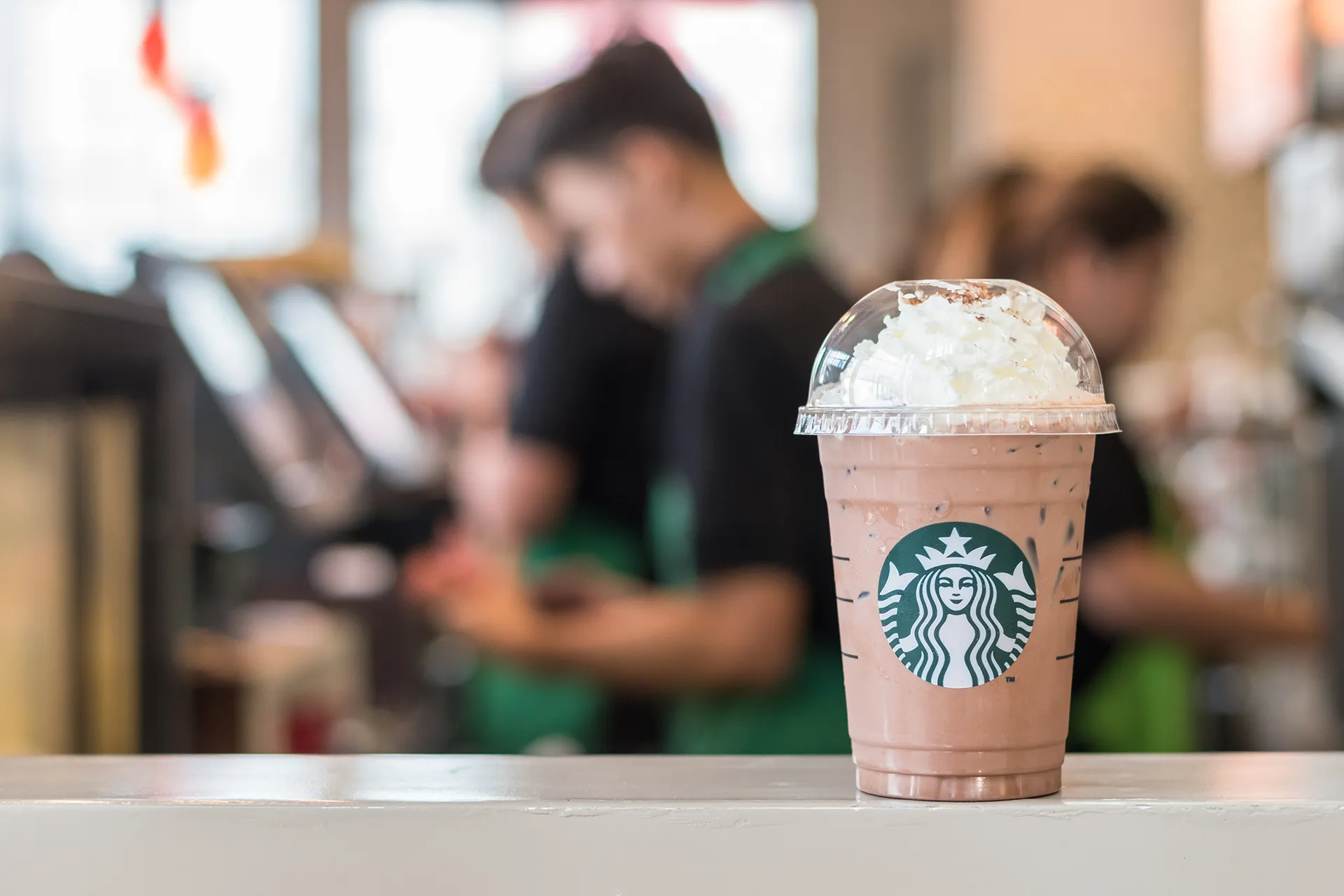Balcão de loja da Starbucks com café em primeiro plano e funcionários em segundo