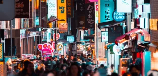 Pessoas andando entre prédios em uma rua iluminada à noite; Seoul, Coreia do Sul