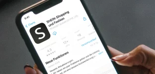 Mão segurando smartphone aberto na página de download do aplicativo do e-commerce de roupas Shein