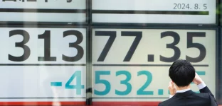 Um pedestre tira uma fotografia de monitores exibindo o número do Nikkei 225 Stock Average do lado de fora de uma empresa de valores mobiliários em 05 de agosto de 2024 em Tóquio, Japão. O índice Nikkei 225 em Tóquio sofreu um declínio significativo, despencando quase 7% em 4 de agosto de 2024, quando caiu para cerca de 33.488,08 pontos logo após a abertura do mercado. (Foto: Tomohiro Ohsumi/Getty Images)