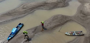 Pessoas carregam bananas caminhando sobre bancos de areia em meio à seca que afeta o Rio Solimões no Amazonas