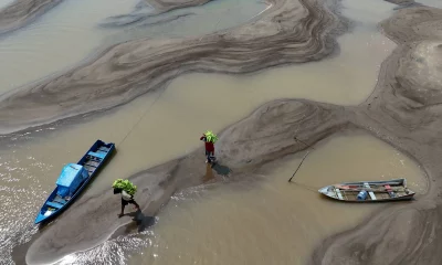 Pessoas carregam bananas caminhando sobre bancos de areia em meio à seca que afeta o Rio Solimões no Amazonas