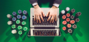 Mãos de jogador online sobre laptop com pilhas de fichas de poker sobre mesa verde de jogo