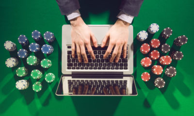 Mãos de jogador online sobre laptop com pilhas de fichas de poker sobre mesa verde de jogo