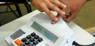 Foto do terminal da urna eletrônica com um dedo sendo colocado sobre o leitor de biometria