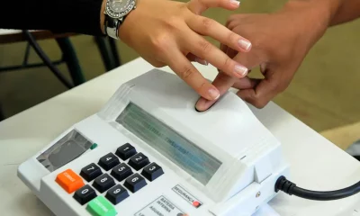 Foto do terminal da urna eletrônica com um dedo sendo colocado sobre o leitor de biometria