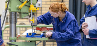 Duas pessoas em macacão azul trabalhando em uma máquina industrial