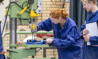 Duas pessoas em macacão azul trabalhando em uma máquina industrial