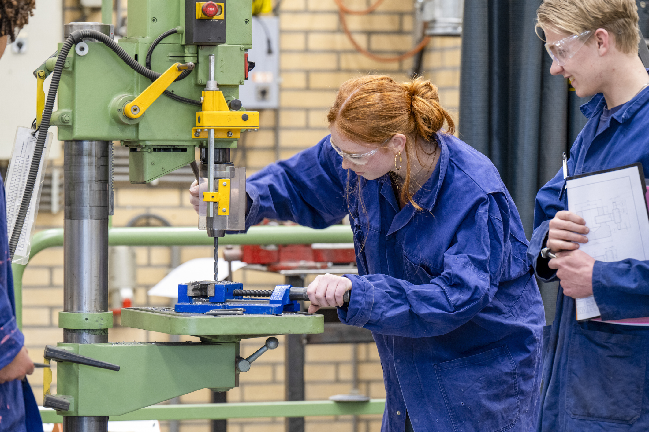 Duas pessoas em macacão azul trabalhando em uma máquina industrial