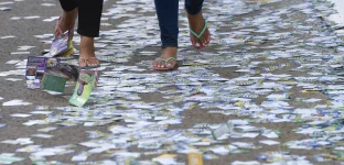 Pessoas andando em calçada cheia de santinhos de candidatos em frente a seção eleitoral