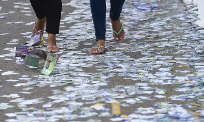 Pessoas andando em calçada cheia de santinhos de candidatos em frente a seção eleitoral