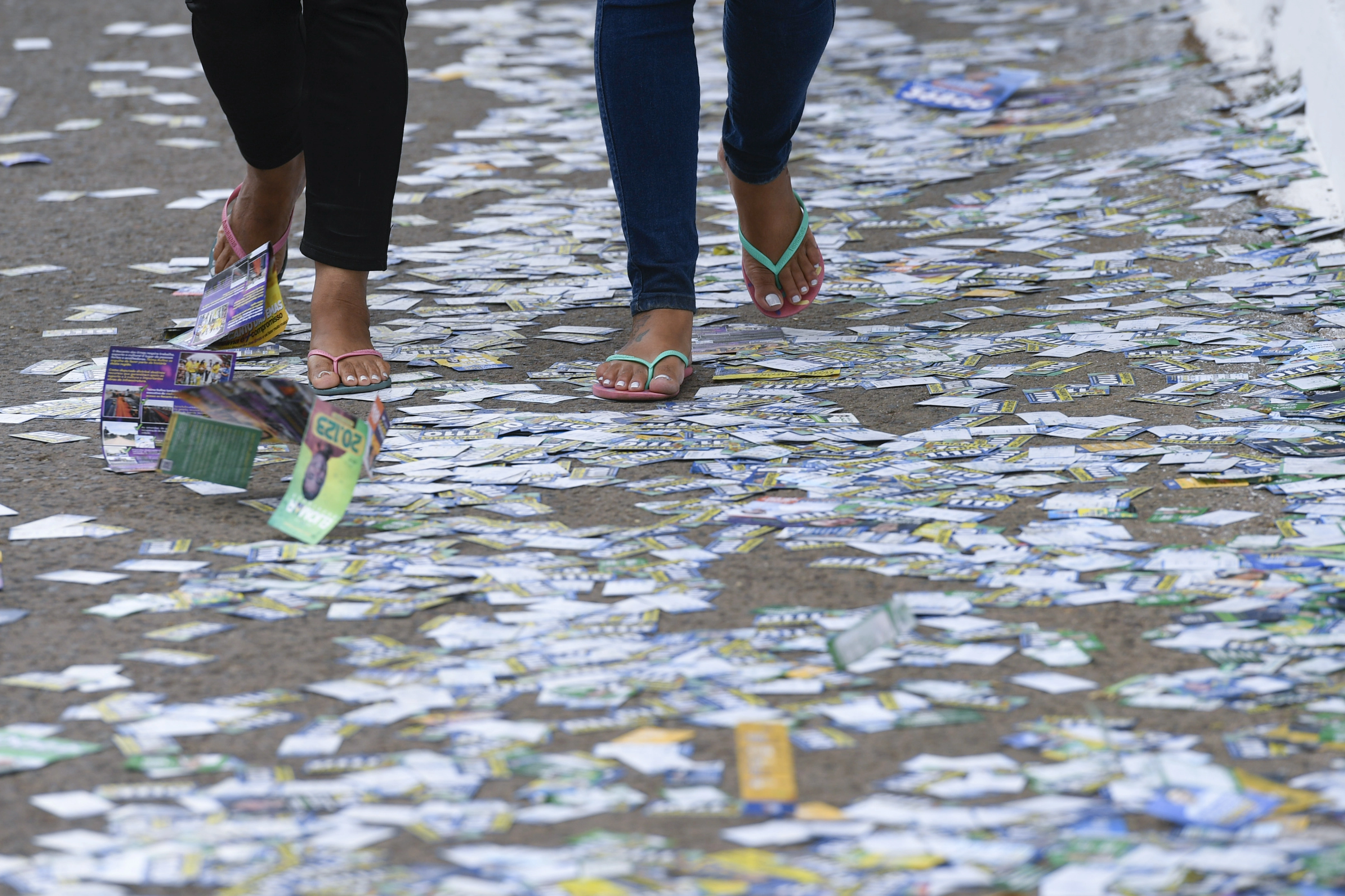 Pessoas andando em calçada cheia de santinhos de candidatos em frente a seção eleitoral