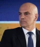 Retrato do ministro do Supremo Tribunal Federal (STF) Alexandre de Moraes, um homem branco e careca, de terno preto, camisa branca e gravata azul escura com padrões discretos está em frente a uma tela digital azul e laranja.