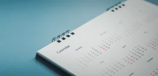 Um calendário de mesa espiral minimalista deitado sobre uma superfície plana com fundo azul.