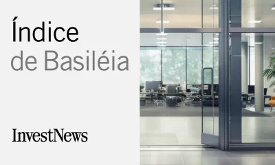 Na imagem apresentada, à esquerda, temos "Índice de Basileia" em letras grandes e estilizadas sobre fundo branco com a logomarca "InvestNews" abaixo; à direita, uma fotografia de um ambiente corporativo moderno e iluminado, com mesas, cadeiras e computadores visíveis através de portas de vidro.