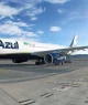 A imagem mostra um avião da companhia aérea Azul estacionado na pista de um aeroporto em um dia claro, com céu azul e algumas nuvens.