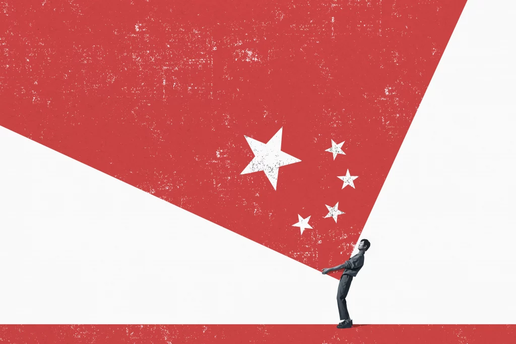 Figura humana em preto e branco segura uma superfície triangular branca contra um fundo vermelho com estrelas, remetendo à bandeira da China.